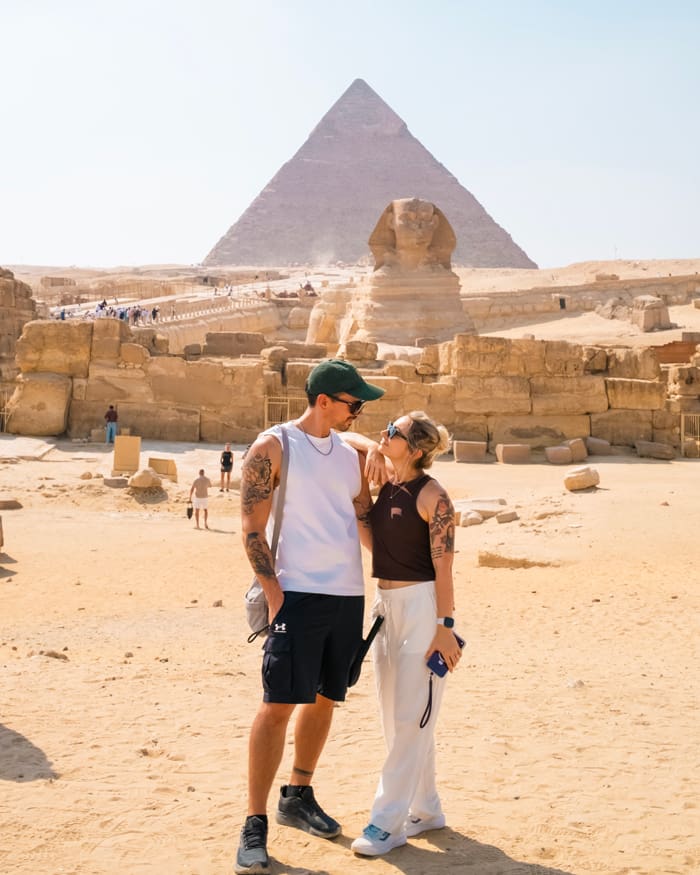 Couple posing in front of the Great Pyramid of Giza and the Sphinx in a sandy desert setting outside Cairo.