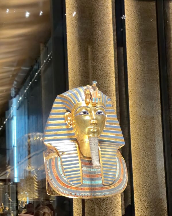 Gold pharaoh bust (Tutankhamun style) with blue-gold striped nemes headdress in a store window.